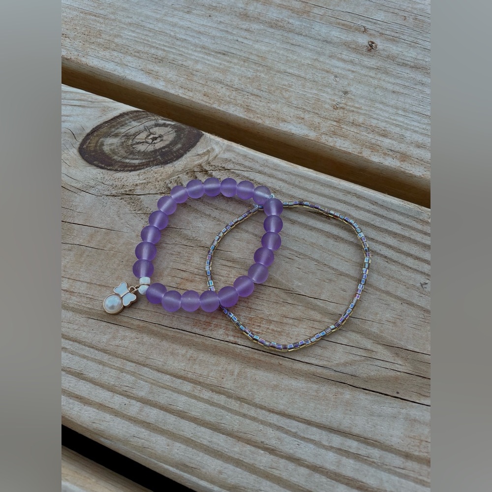 Two beaded bracelets, one with a charm. Both purple and same size